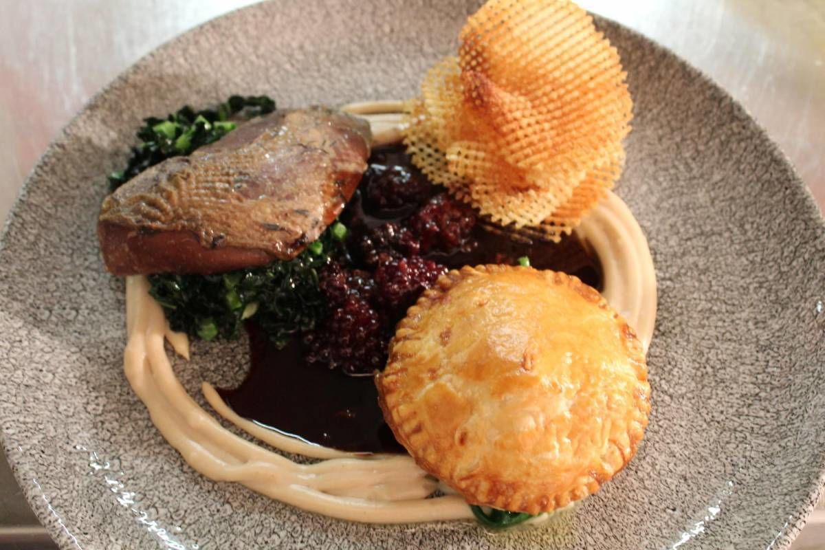 Une assiette contenant un morceau de viande, une pâtisserie et une sauce brune.