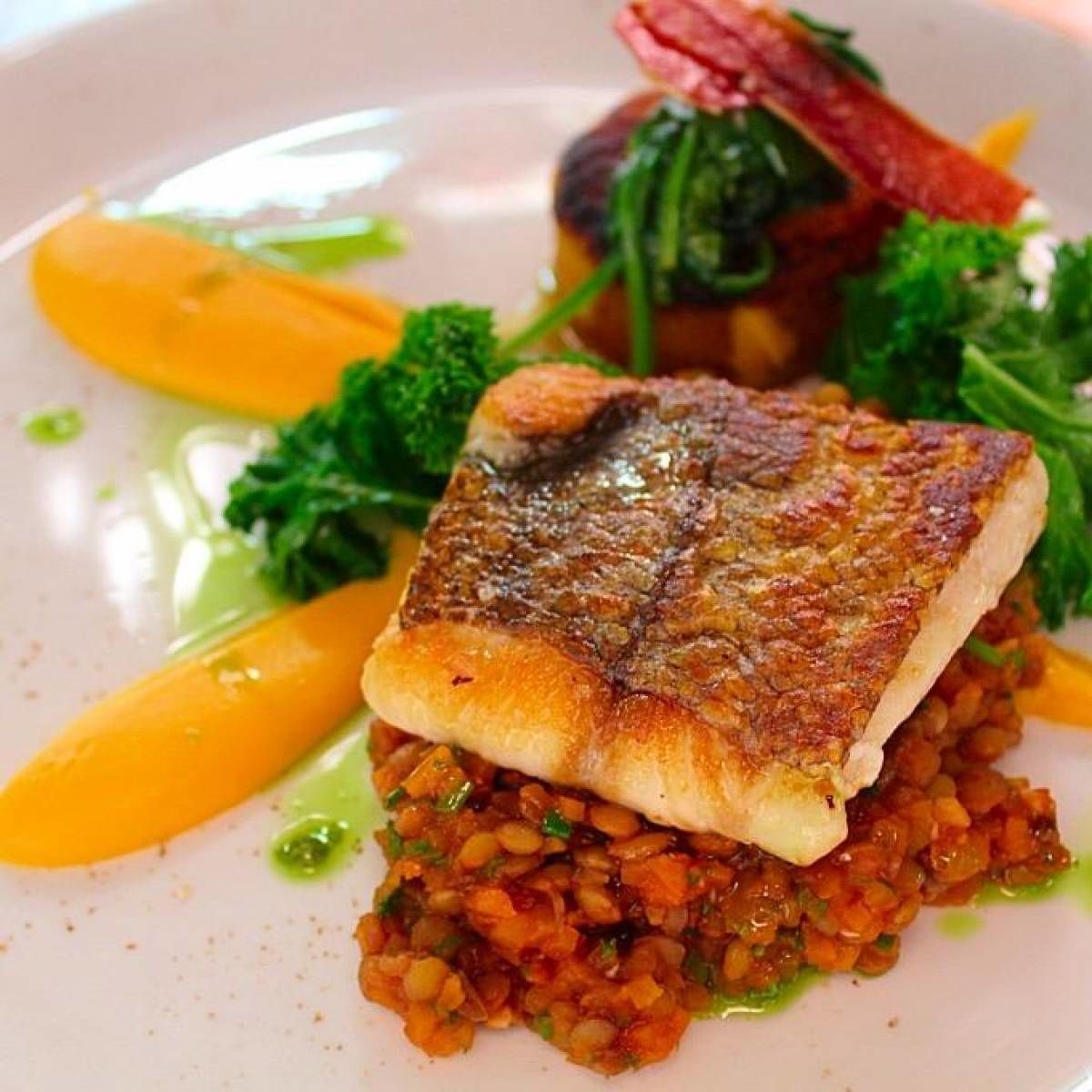 Un plato con un trozo de pescado, verduras y salsa.