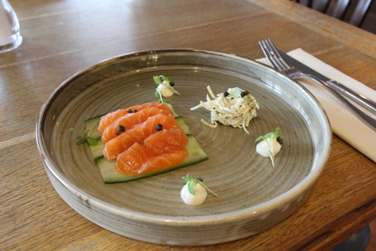 A plate with salmon, cucumber, and garnishes on a ceramic dish.