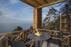 Une terrasse en bois avec une table ronde et deux chaises, offrant une vue panoramique sur l’océan et la forêt.