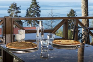 Une table avec deux pizzas, des salières et des poivrières, et des verres, le tout disposé devant un paysage pittoresque composé d’arbres et d’eau.
