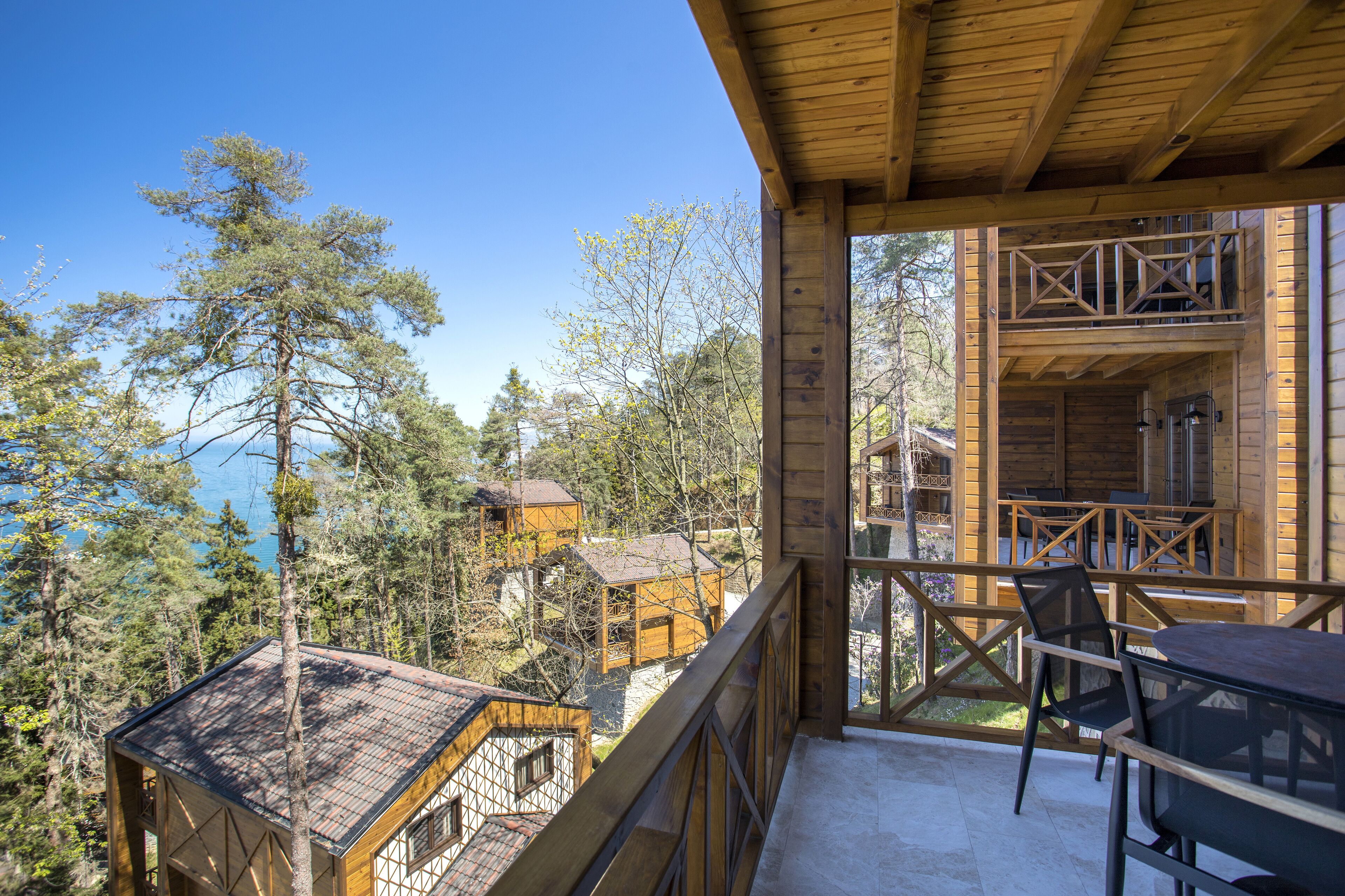 A wooden cabin with a balcony overlooking a forest and a lake.