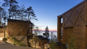 Une cabane en bois, accessible par un sentier de pierres, entourée d’arbres et offrant une vue sur une étendue d’eau.