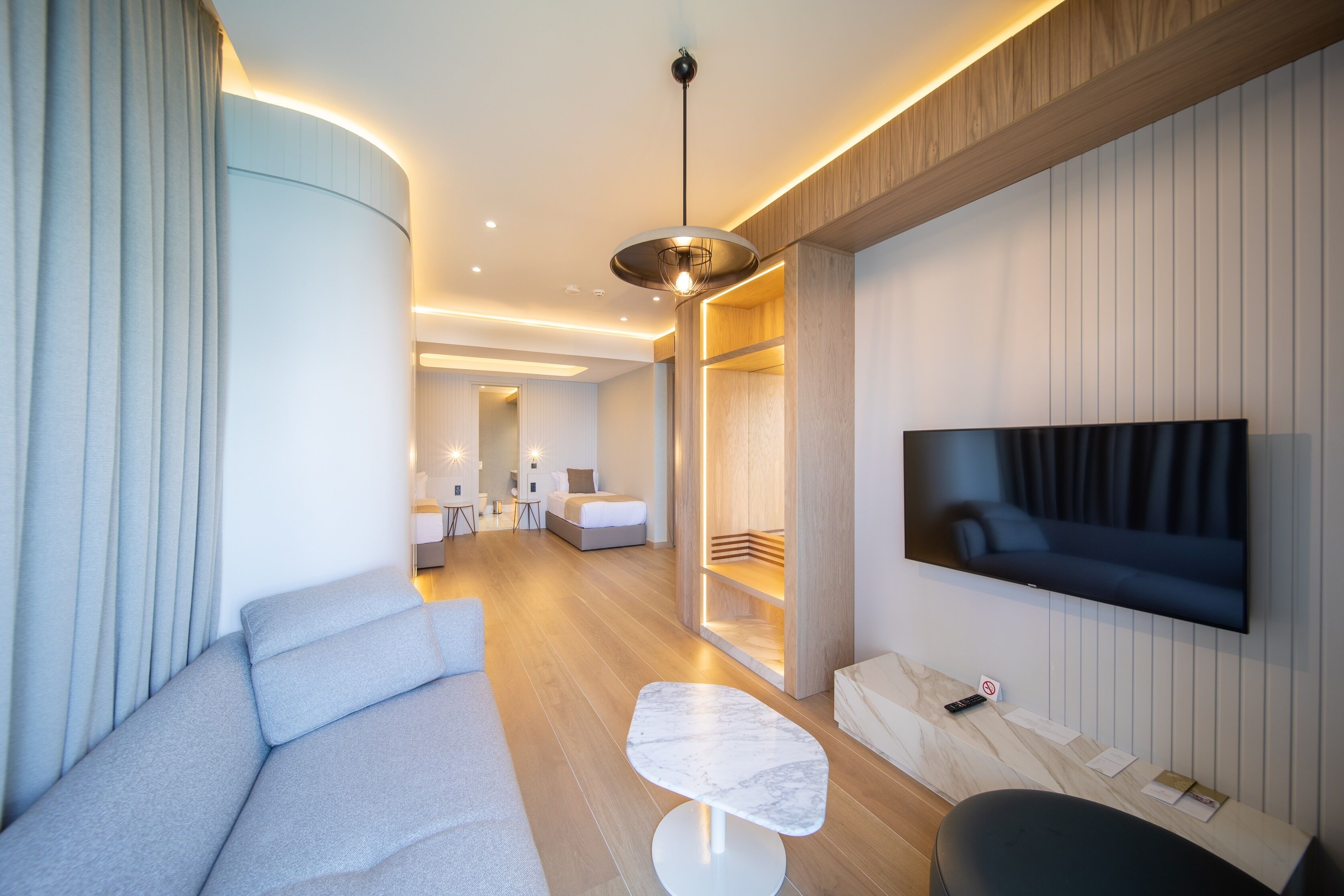A modern hotel room with a large flat-screen TV, a sofa, a small table, and a wooden accent wall.