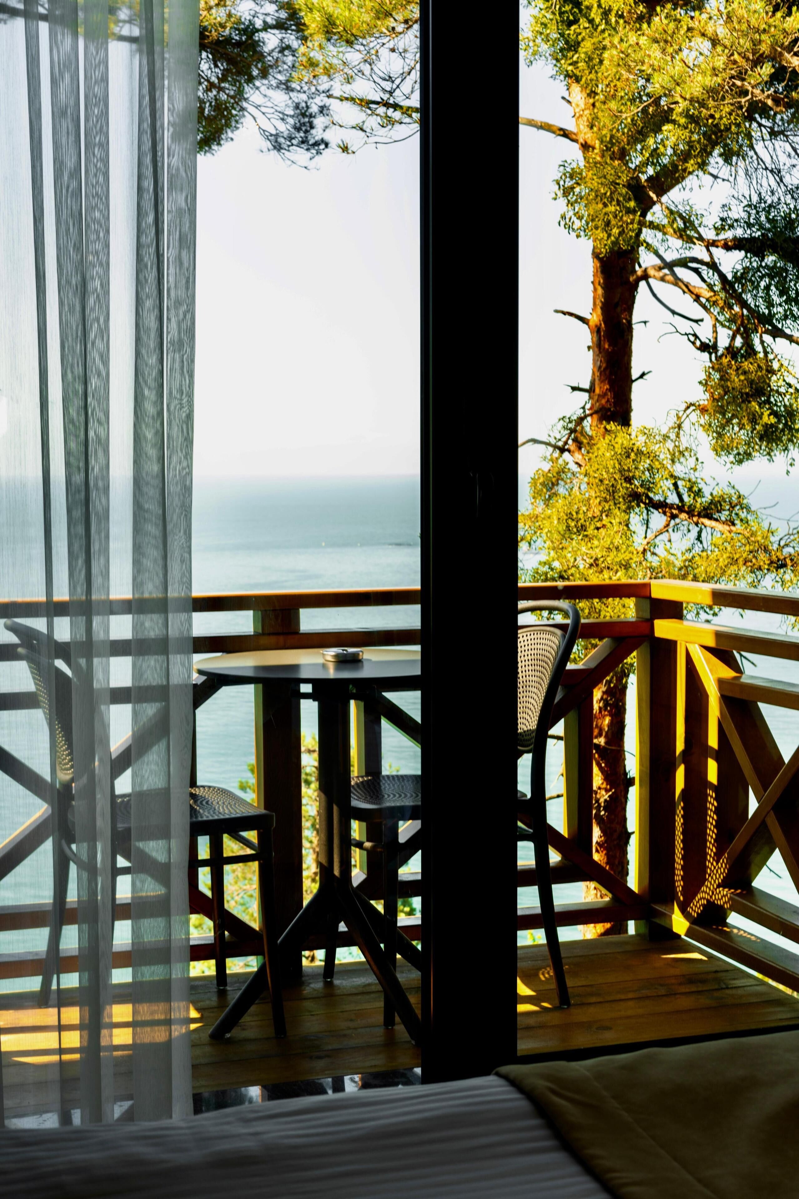 A balcony with a view of the sea, a table, and chairs.