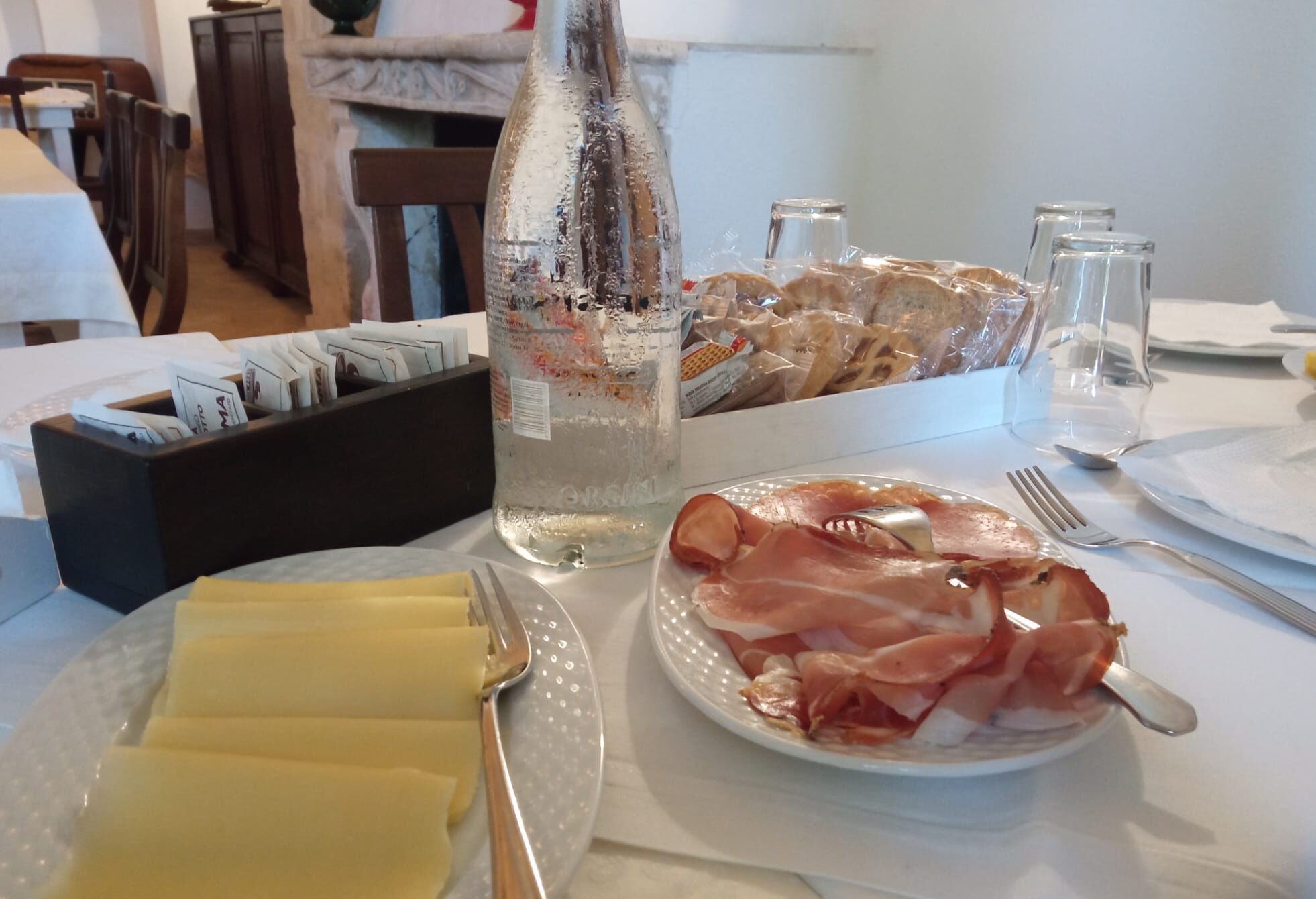 Ein Tisch gedeckt mit einer Wasserflasche, Parma-Schinken und einem Servietttuch.