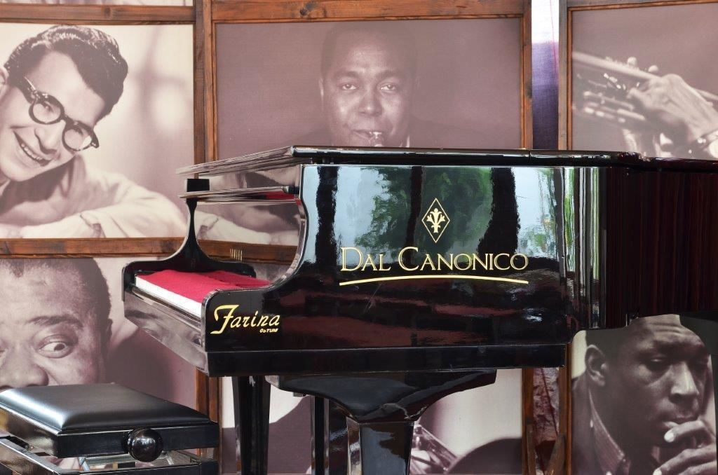 A black Dal Ciconico piano with a red music stand, set against a backdrop of framed black and white photographs.