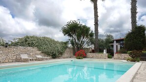 Una piscina con lettini, circondata da mura in pietra e diverse piante.