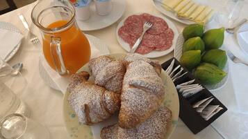 A breakfast setting with croissants, sliced salami, fresh fruit, and a glass of orange juice.