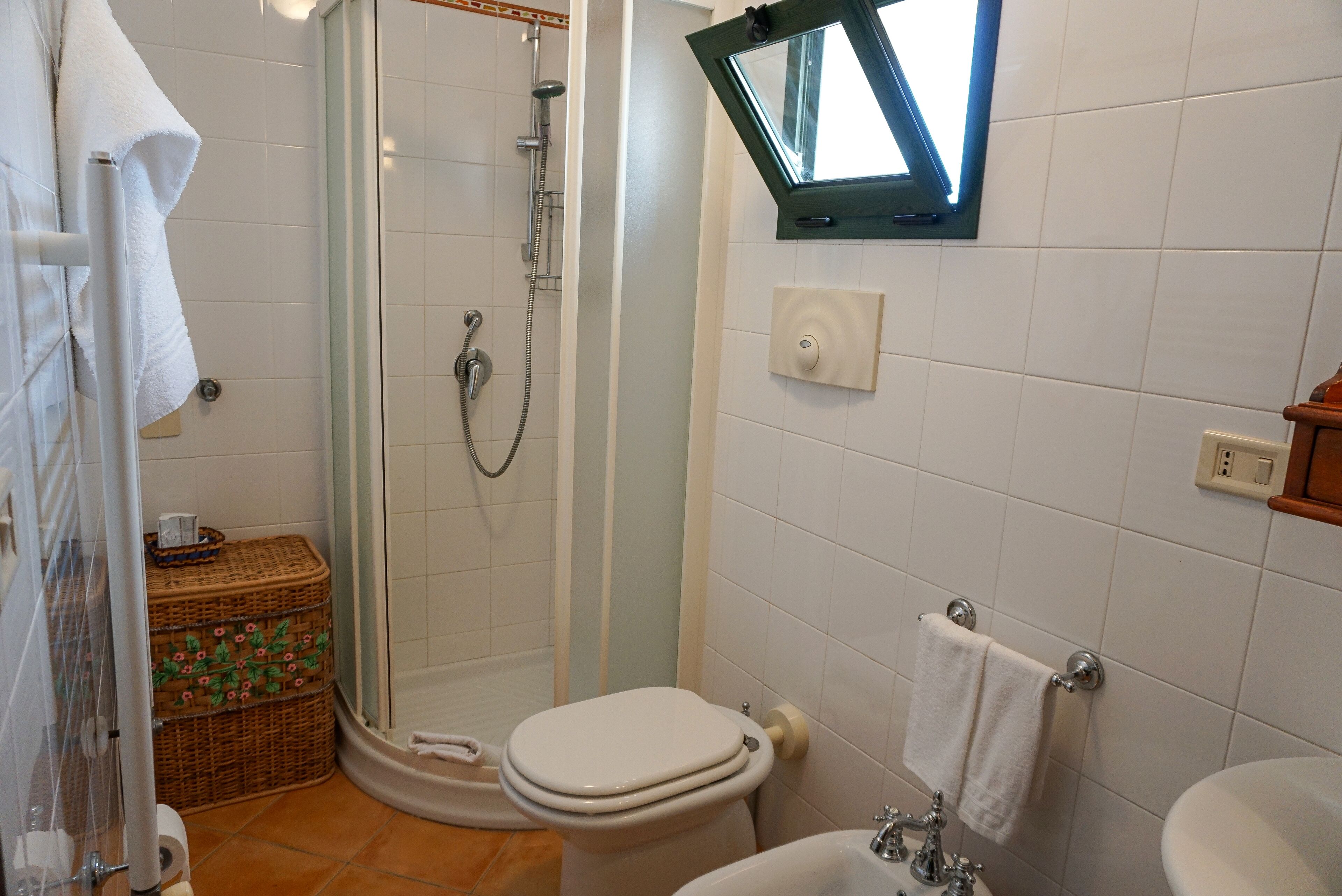 Een badkamer met douche, toilet, wastafel en een raam.