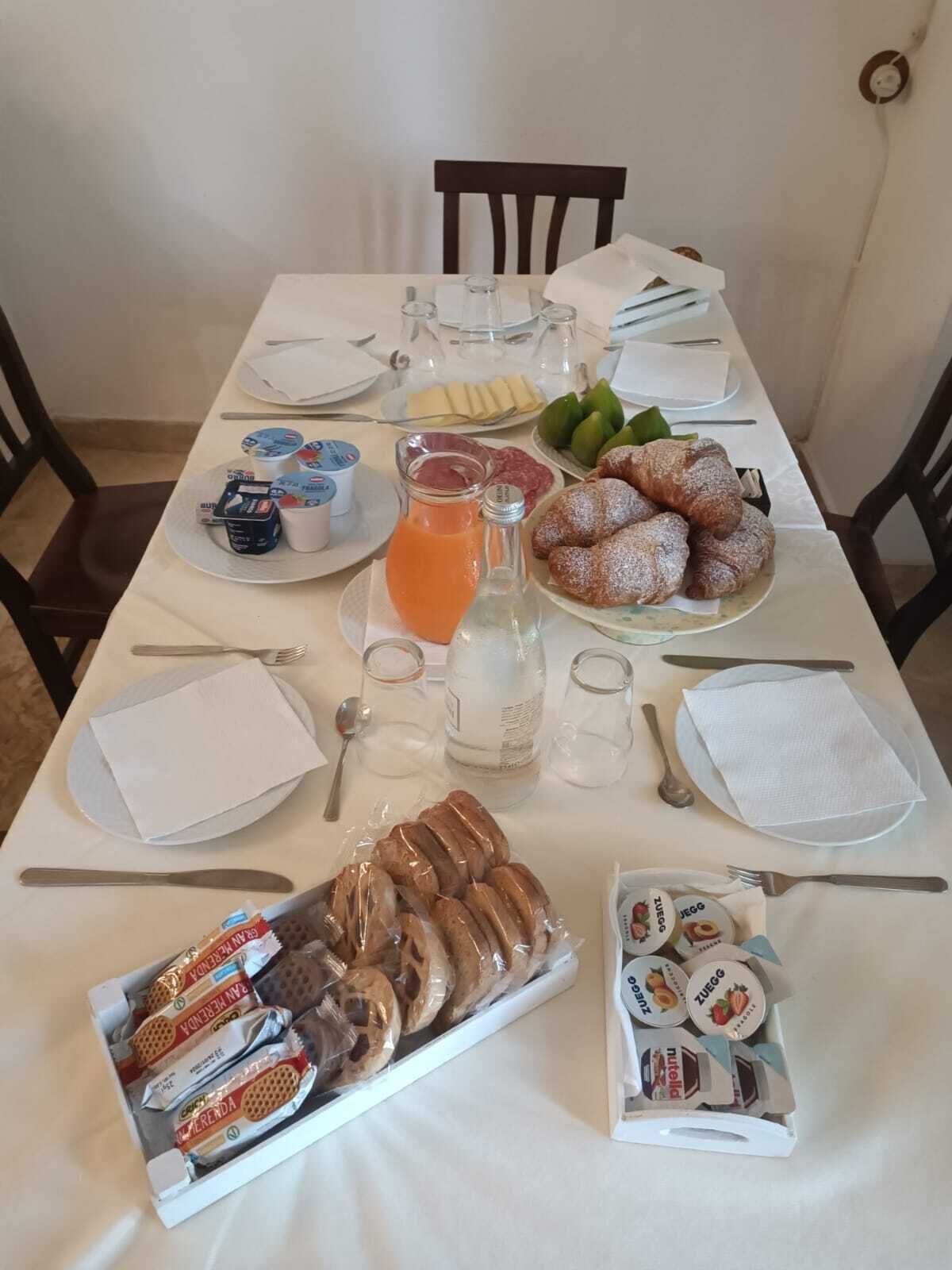 A breakfast table set with plates of pastries, a pitcher of orange juice, and various condiments.