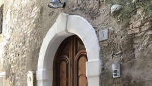 Um edifício de pedra com uma grande porta de madeira dupla, uma entrada em arco e uma pequena luminária acima da porta.