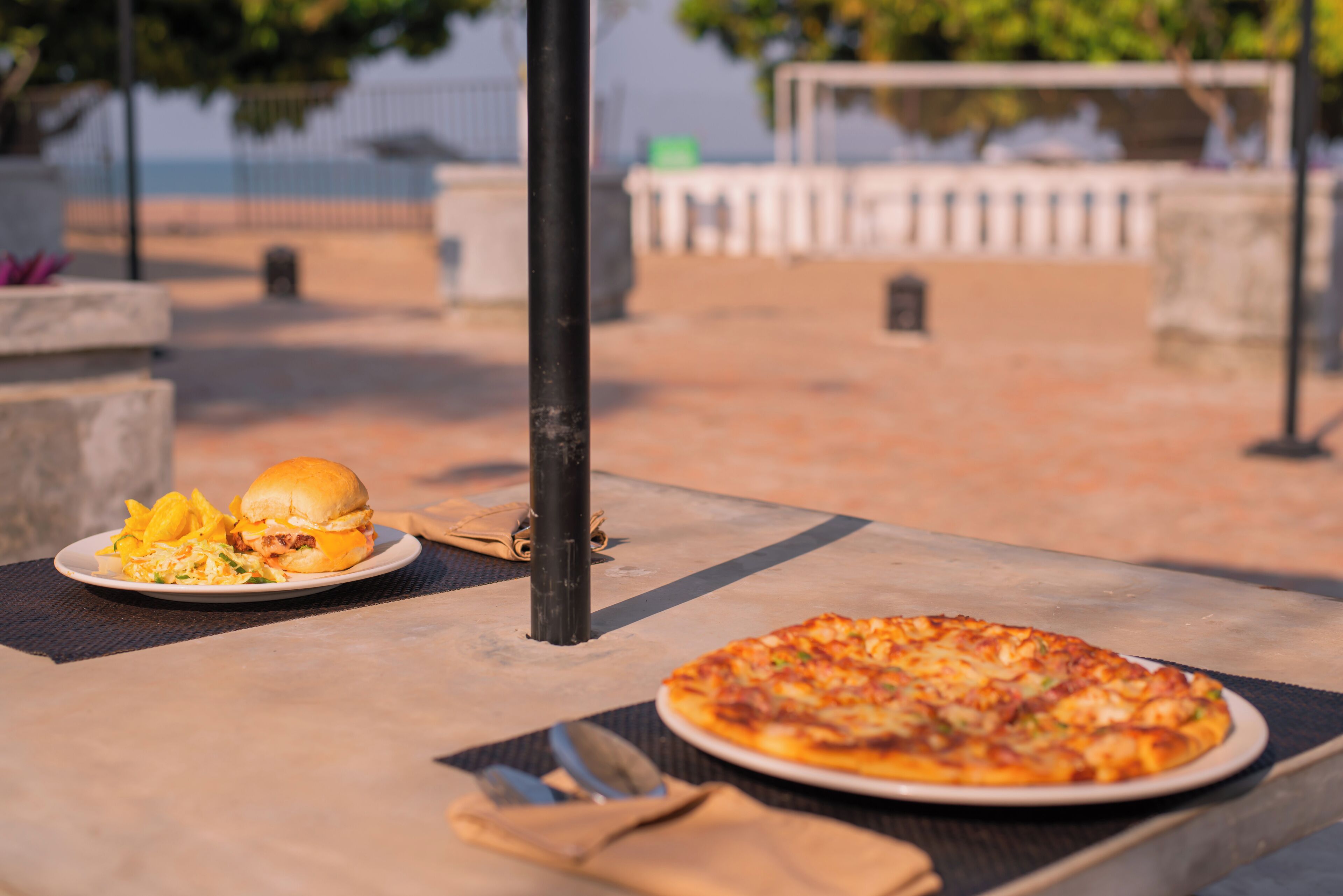 Uma mesa com pizza, um hambúrguer, um guardanapo e um garfo.