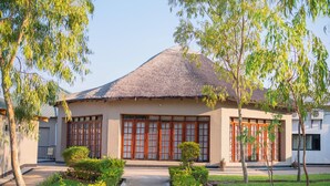 A building with a thatched roof, large wooden sliding doors, and a garden with trimmed bushes and trees.