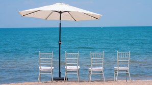 A beach with three white chairs and a white umbrella.