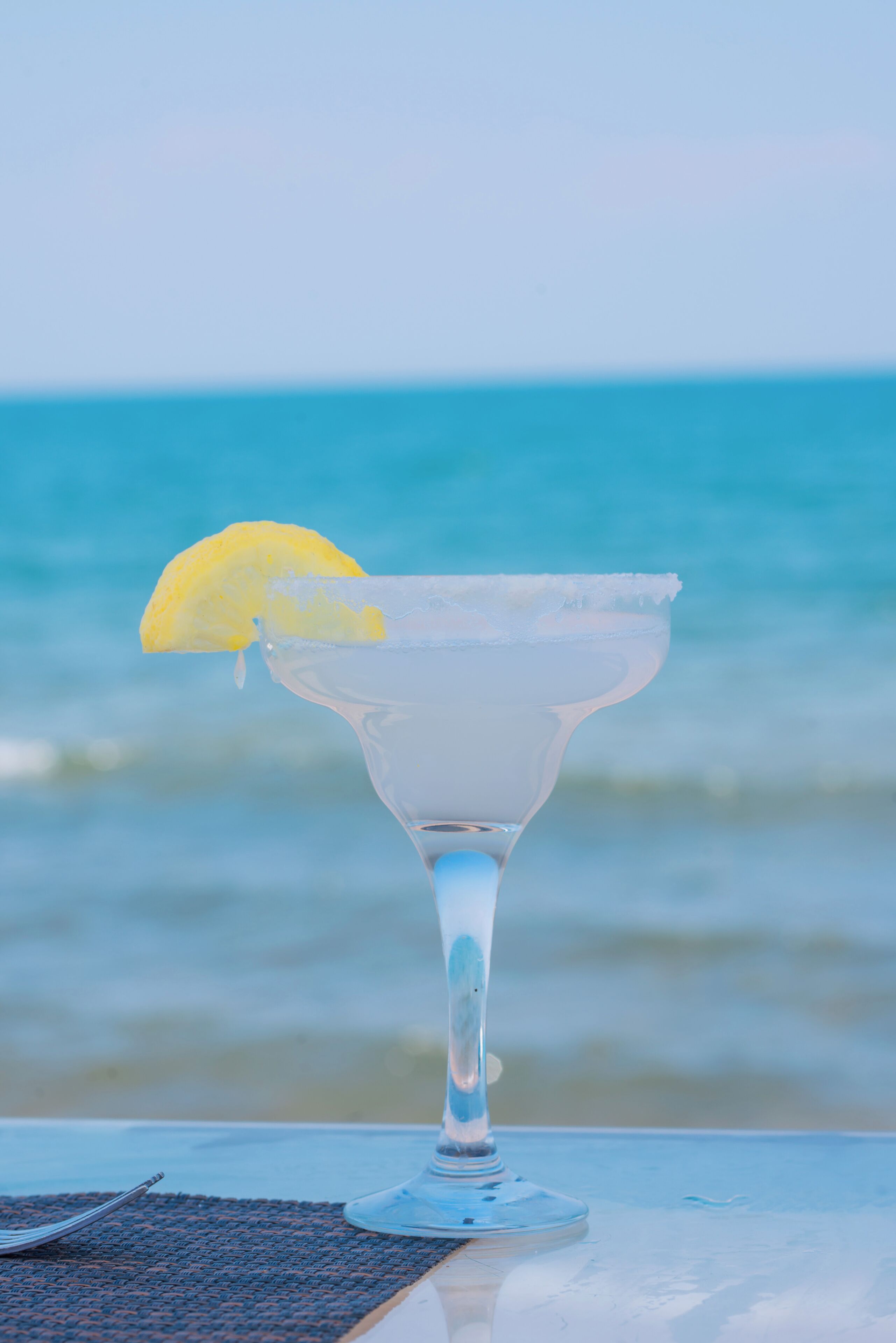 A clear glass with a lemon garnish on a table by the ocean.