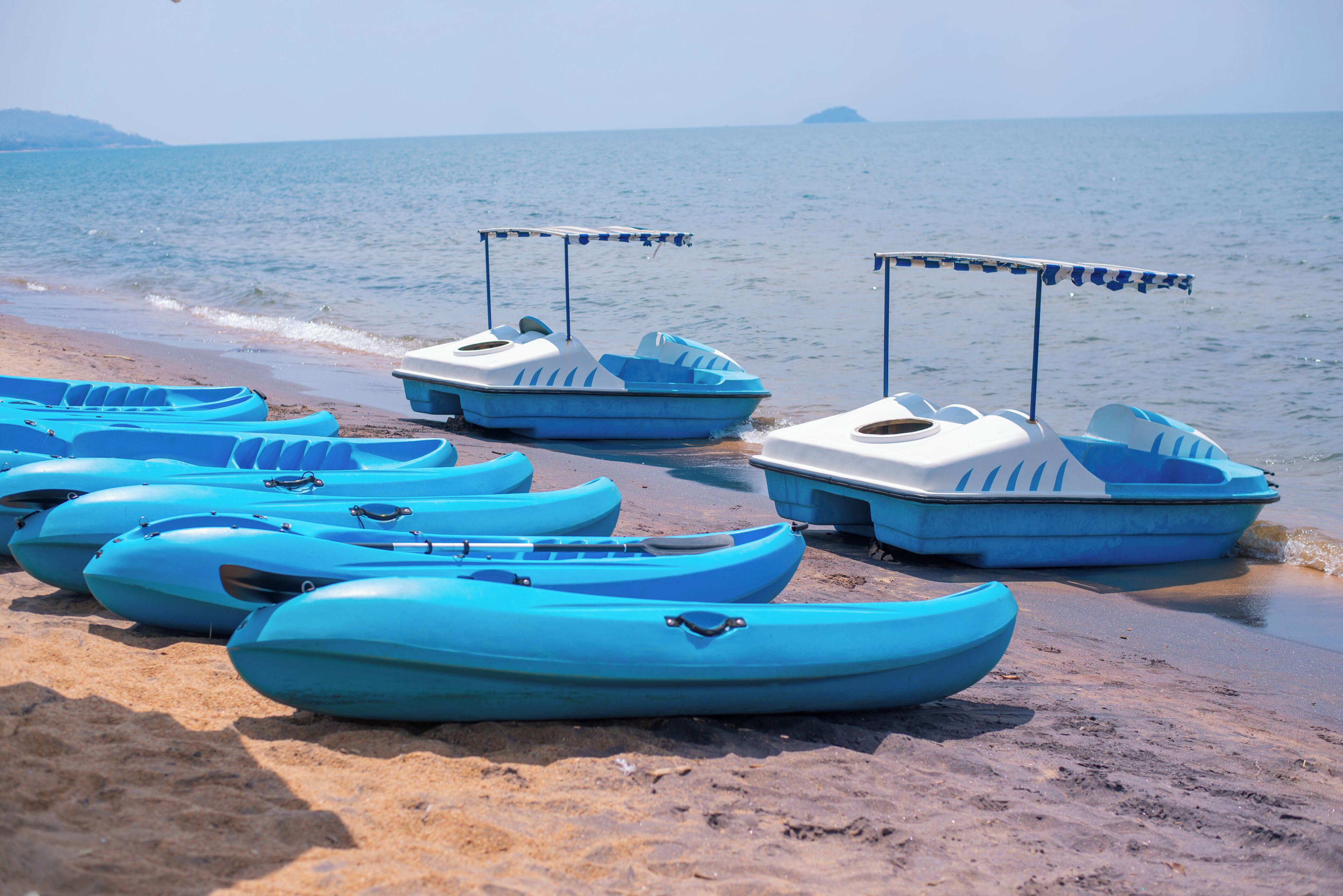 Varias kayaks azules alineadas en una playa arenosa, con el mar al fondo.