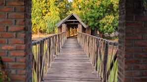 A wooden bridge leading to a brick structure with a triangular roof.
