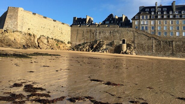 A coastal fortification with a sandy beach in the foreground and a stone wall.