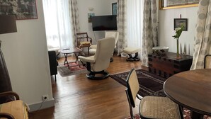 A living room with a wooden floor, a dining table, a sofa, a TV, and a painting on the wall.