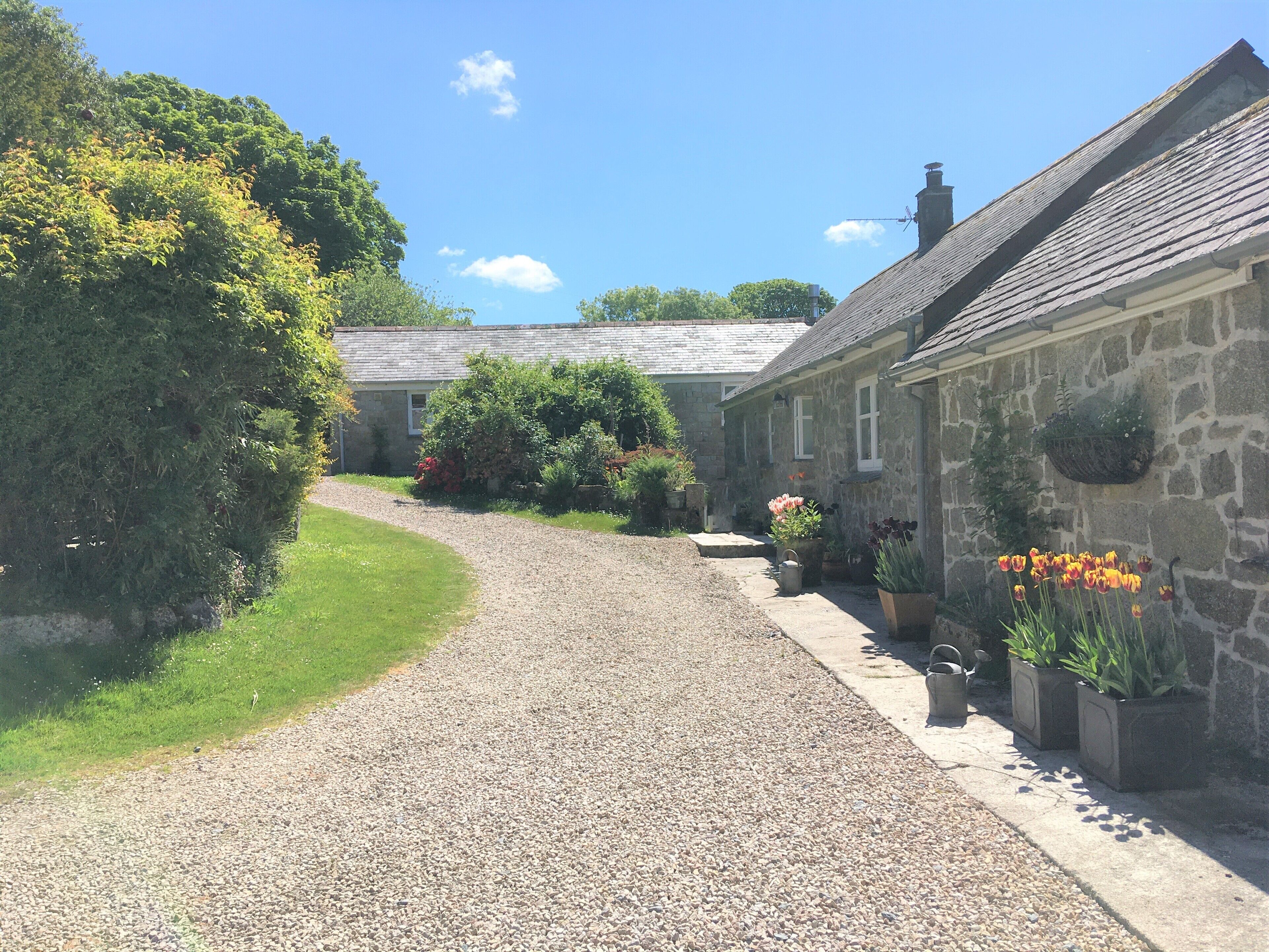 A gravel driveway leading to stone buildings with flower planters.