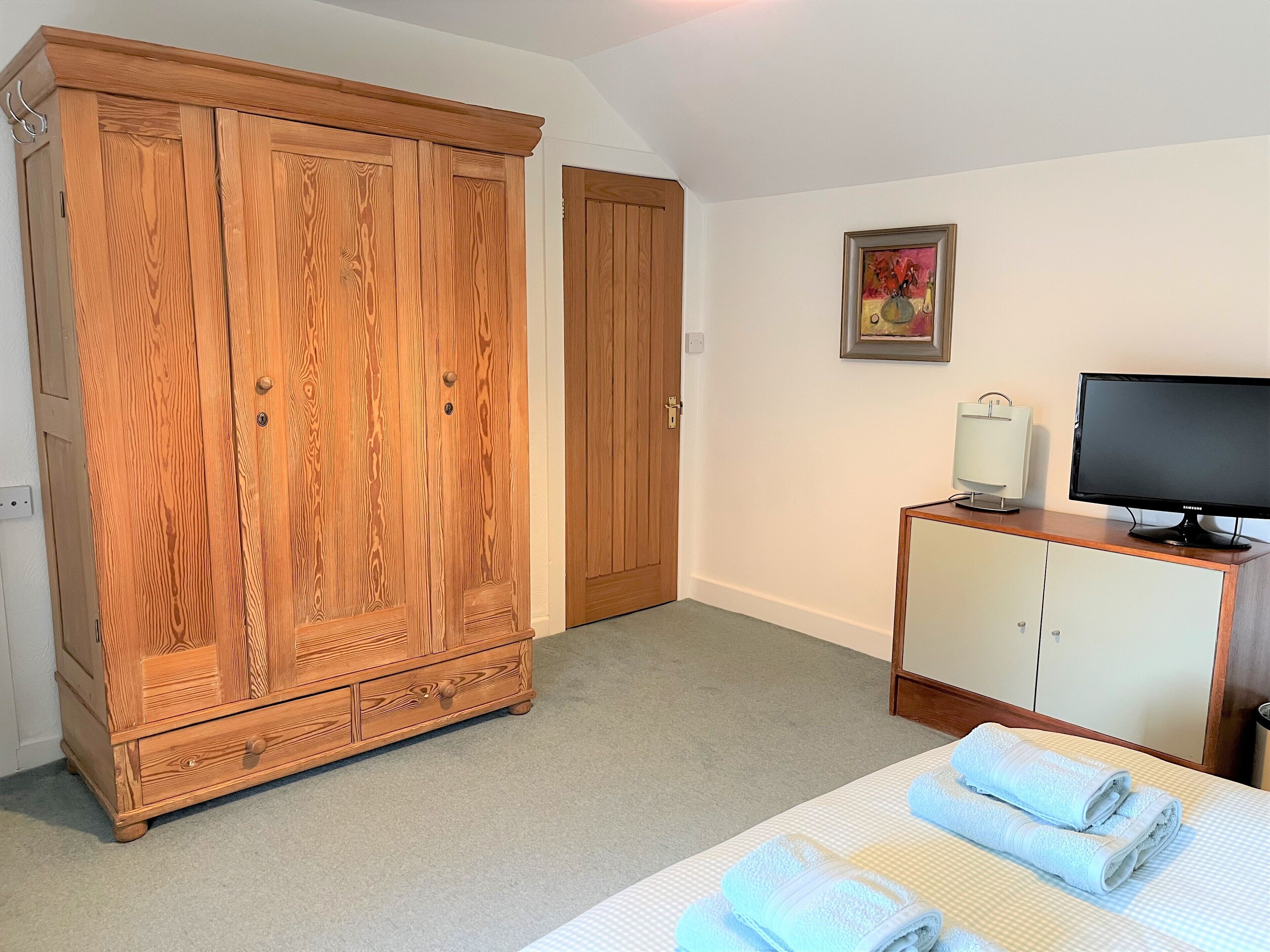 A hotel room with a large wooden wardrobe, a television on a cabinet, and neatly folded towels on the bed.