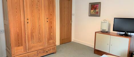 A hotel room with a large wooden wardrobe, a television on a cabinet, and neatly folded towels on the bed.