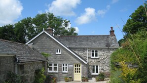 A stone house with a gravel driveway, potted plants, and a clear sky. - Little Pengelly Farm (Hayle)