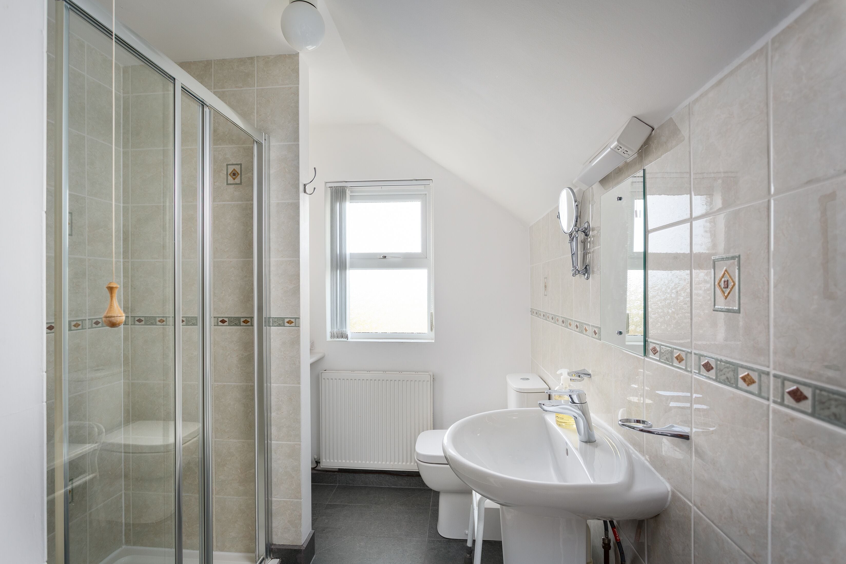 Et moderne badeværelse med en glasbrusekabine, en hvid vask og et toilet.