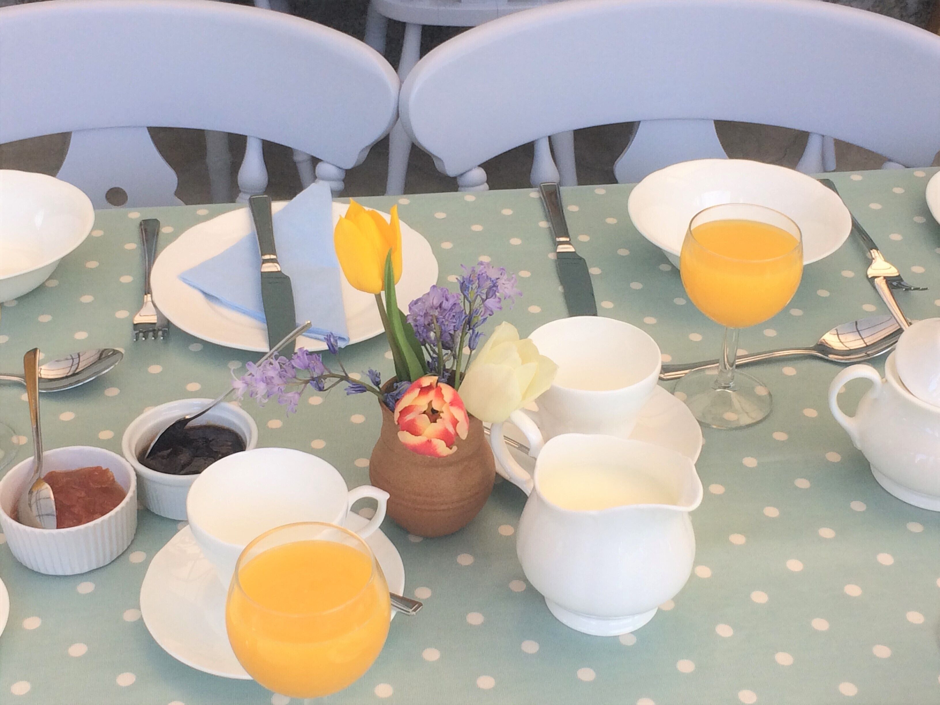 A breakfast table set with plates, cups, and a vase of flowers.
