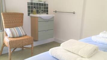 A bedroom with a bed, a chair, a bedside table, a mirror, and a bathroom with a sink and a towel rack.