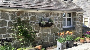A stone building with a window, a flower box, and potted plants. - Little Pengelly Farm (Hayle)