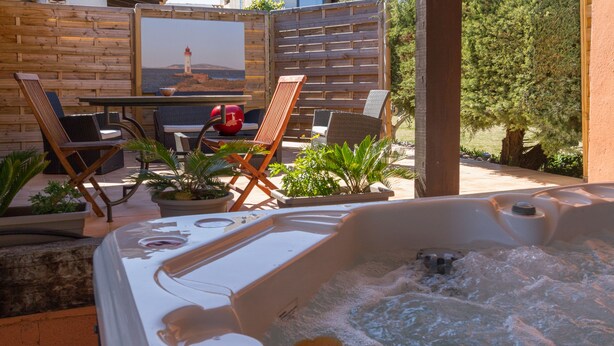 A hot tub with a wooden deck and chairs, a table with a bowl, and a painting of a lighthouse. - La chambre des Onglous (Marseillan)