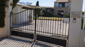 A gated entrance with a stone wall and a metal gate. - La chambre des Onglous (Marseillan)