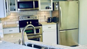A kitchen with stainless steel appliances, white cabinets, and a marble countertop.
