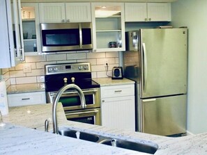 A kitchen with stainless steel appliances, white cabinets, and a marble countertop.
