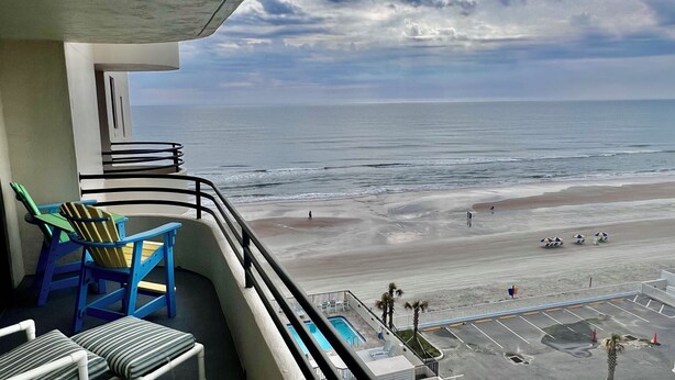 A balcony with chairs, a pool, and a view of the beach and ocean.