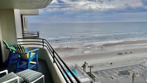 A balcony with chairs, a pool, and a view of the beach and ocean.