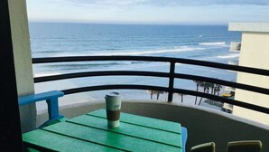 A balcony with a green table and chairs, overlooking the ocean.