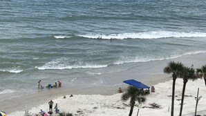 A beach with people, palm trees, and a blue umbrella.
