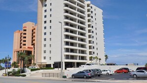 A multi-story hotel with balconies, a parking lot, and palm trees.