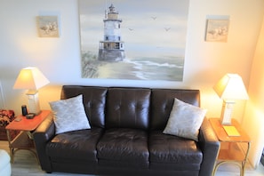 Relax in this inviting living room with a leather sofa, side tables, and a beautiful lighthouse painting.