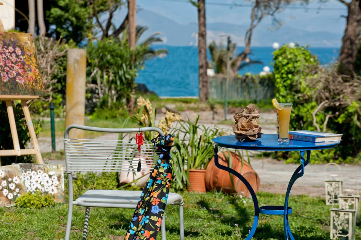A garden with a metal bench, a table with a drink, and a painting in the background.