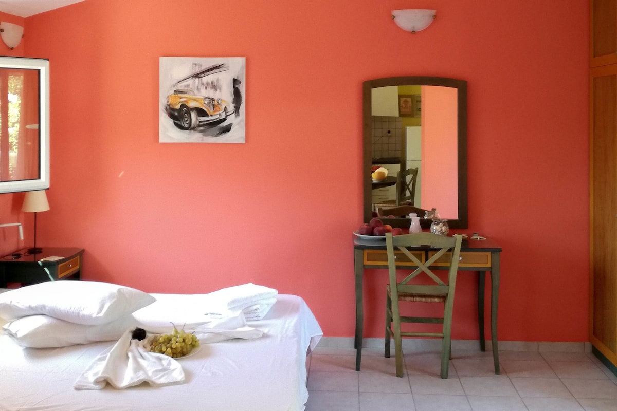 A hotel room with a bed, a desk, a chair, a mirror, and a painting on the wall.