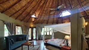 Una habitación con techo de paja, una cama con dosel, un sofá, una mesa y una lámpara.