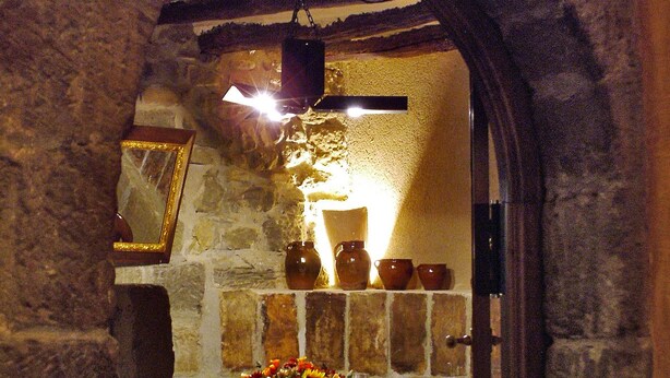 Un comedor interior con una pared de piedra, una mesa de madera dispuesta con platos, vasos y un florero.
