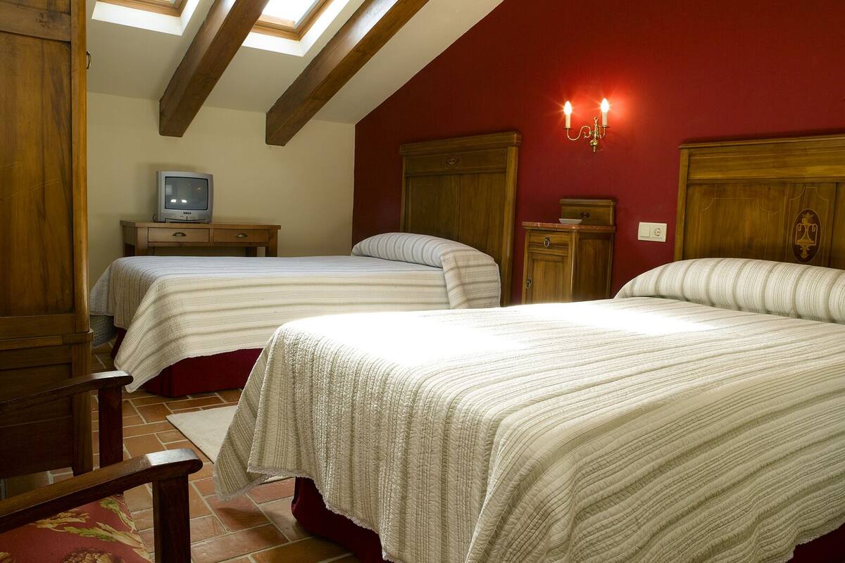 Un dormitorio con dos camas, vigas de madera, un tragaluz, un televisor y una mesita de noche.