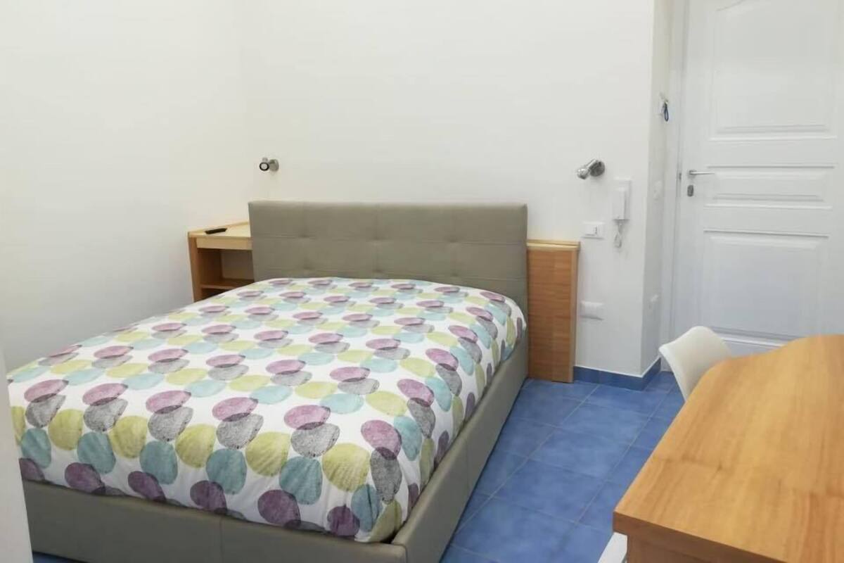 A bedroom with a bed, bedside tables, a wooden desk, and a door.