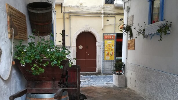 Un estrecho callejón con un barril de madera, una planta en maceta y una puerta al fondo.