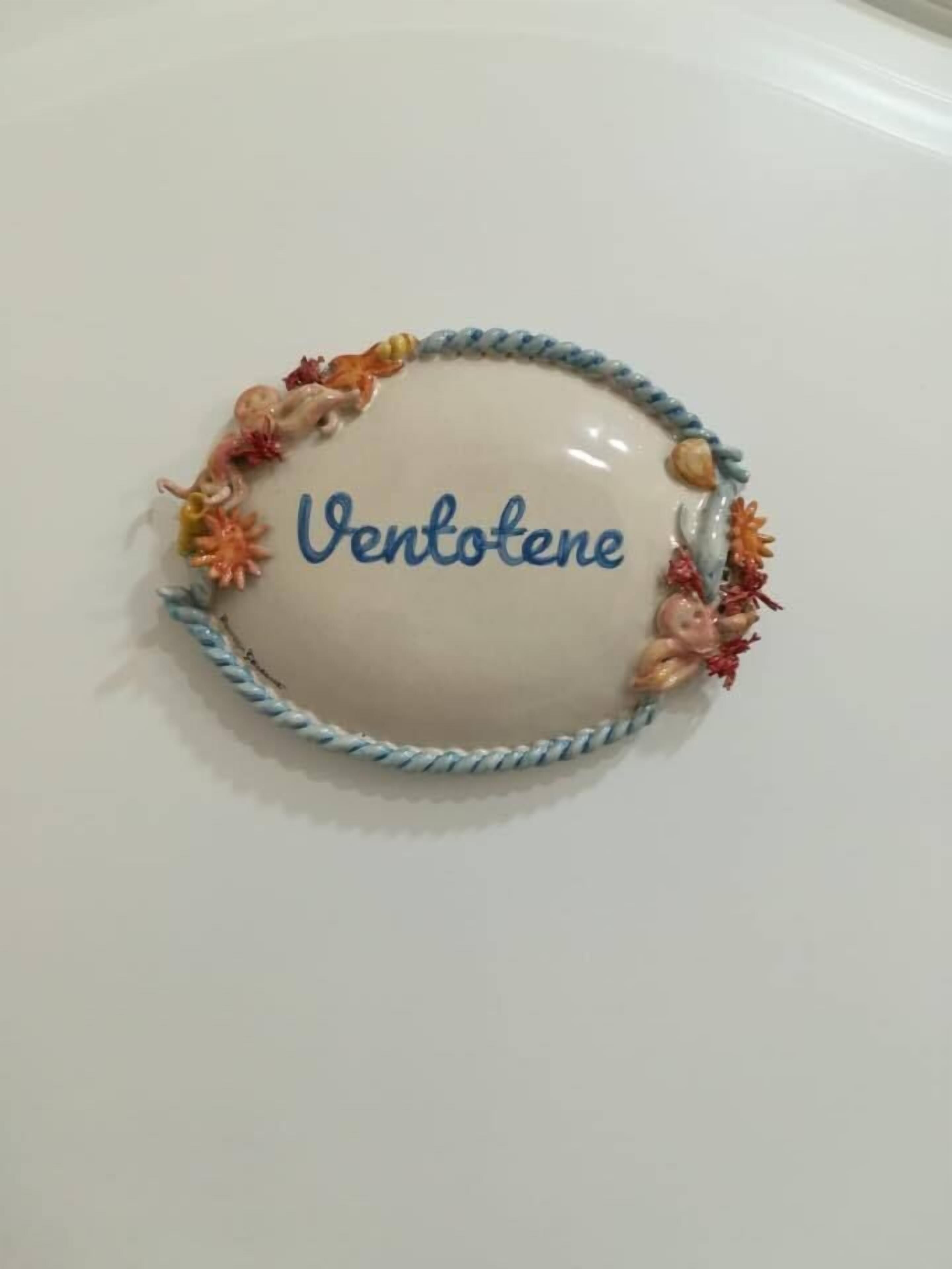 A white table with a decorative item featuring the name "Ventotene" and a braided border with colorful beads.